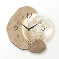 A modern wall clock with a moon and rock design, featuring a textured beige stone face, a glowing moon phase center, black hands, and irregular stone-shaped cutouts around the edge on a white background.