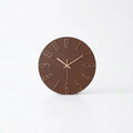 A minimalist round wall clock with a dark brown face and light beige numerals and hands.